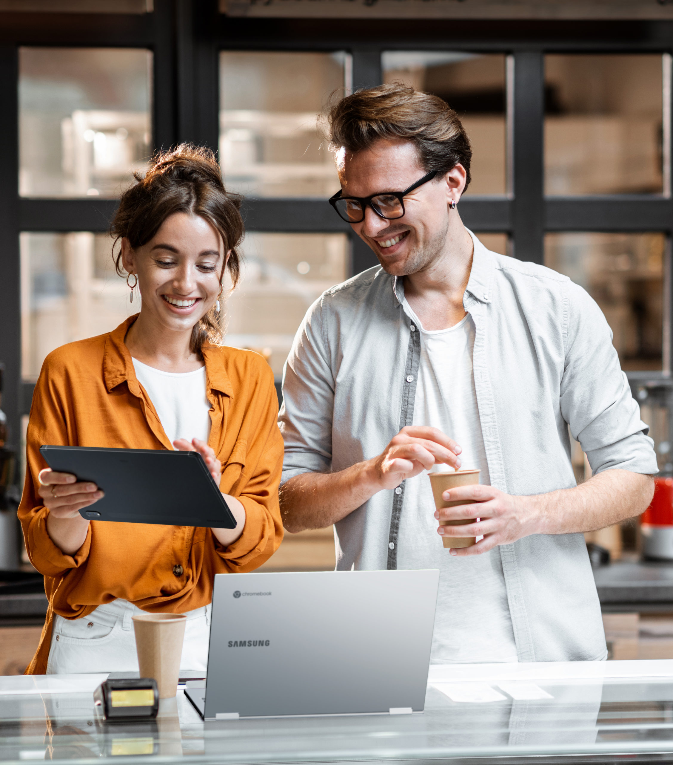 Two young managers or shop owners having some discussion while standing with a digital tablet at the counter of the shop or cafe. Small business management concept